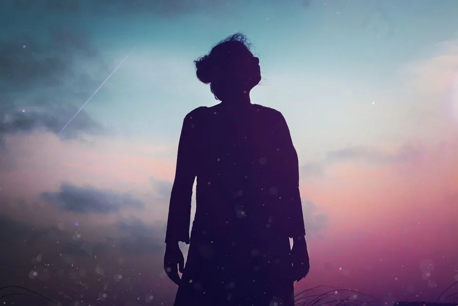 A silhouette of a woman gazing into the colorful twilight sky, evoking mystery and dreams.