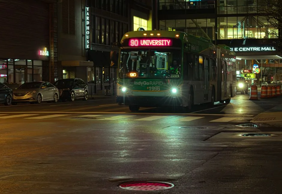 City bus on University route at night in urban setting with illuminated streets and buildings.