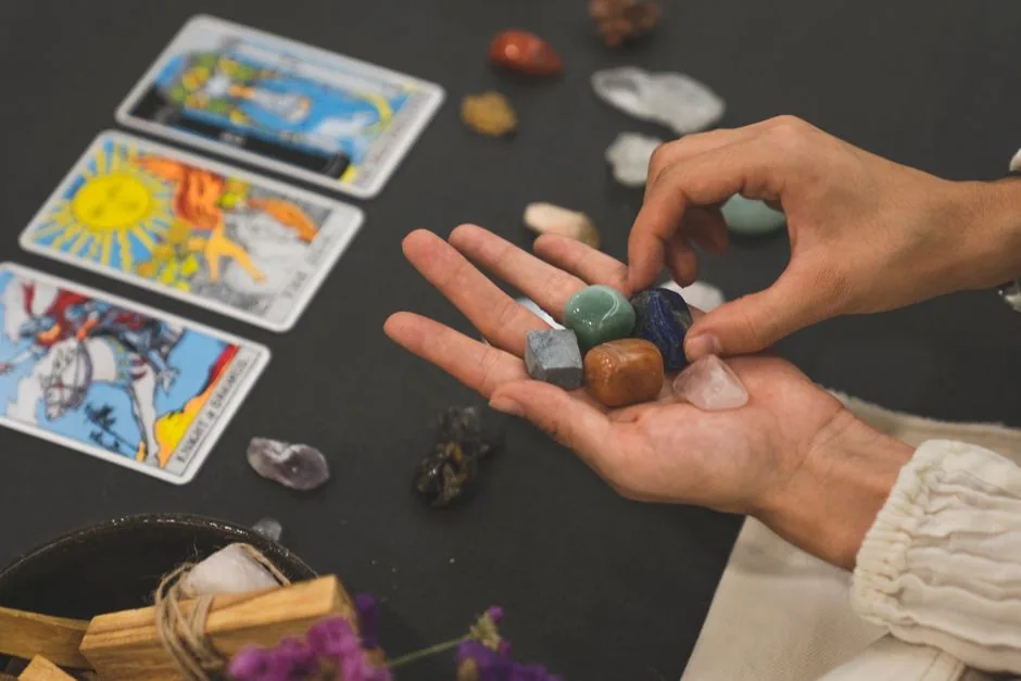 Person holding healing crystals with tarot cards in the background, symbolizing spirituality.