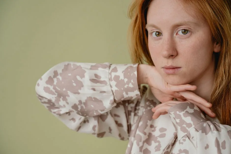 Close-up portrait of a woman with red hair and patterned blouse in a studio setting with soft lighting.