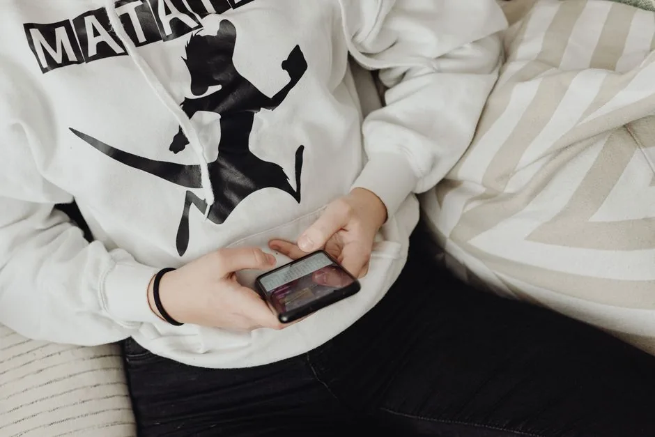 Close-up of a person using a smartphone in a casual hoodie while seated indoors.