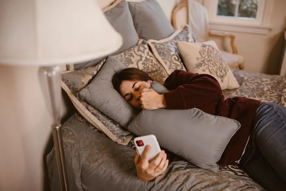 A young woman lying on a bed, holding a phone and a pillow, symbolizing relaxation and connection.
