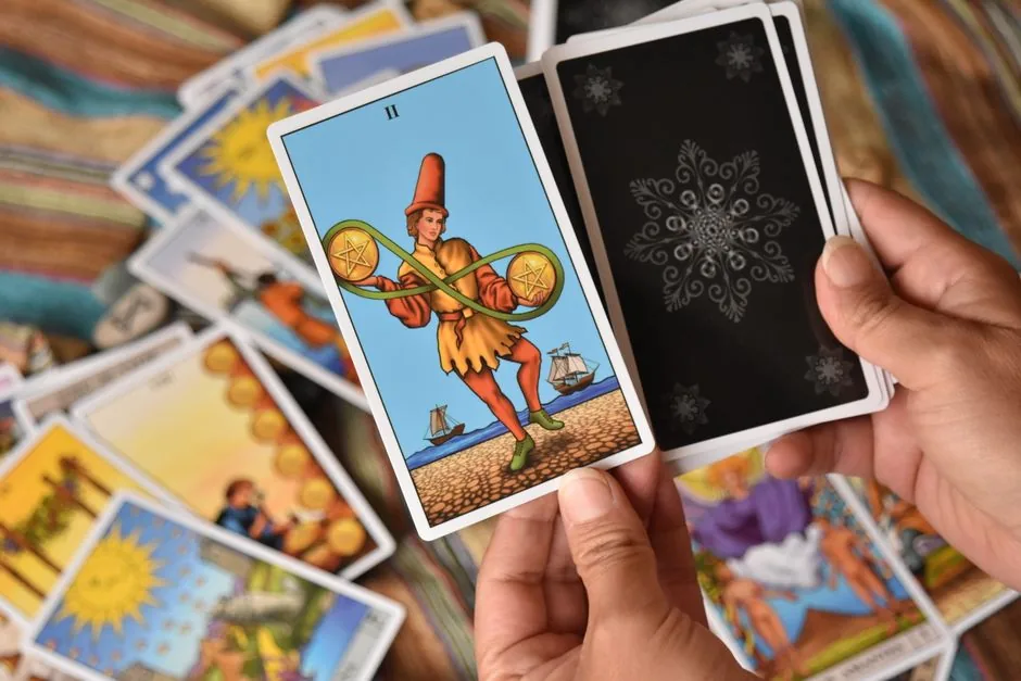 Hands holding a tarot card with a deck spread out, suggesting divination or fortune-telling.
